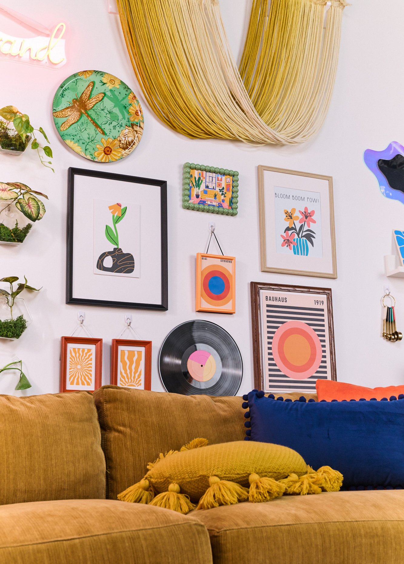 Dorm room seating area with a mustard yellow loveseat, wall mounted greenery, and colorful wall art