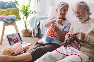 Woman teaching man to knit wool with needle at home