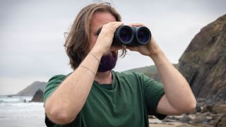 A male using the Canon 15x50 IS binoculars with the sea and coastline behind them.