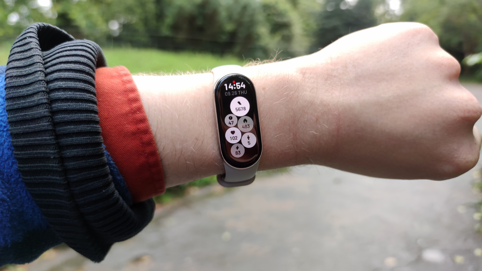 The Xiaomi Smart Band 9 on a man's wrist in front of a green park.