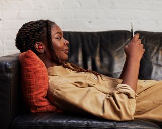 Woman relaxing on the sofa wearing Beats Studio Buds in red