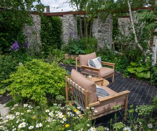 A garden designed for the RHS 2024 Chelsea Flower Show with a set of garden armchairs and reclaimed stone columns