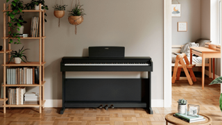 Black Yamaha digital piano in a living room with hanging plants above it