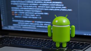 Google Android figure standing on laptop keyboard with code in background