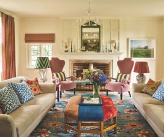 living room with patterned rug and cream sofas and pink armchairs and white walls