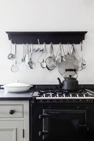 kitchen detail with black range cooker and black shelf above on white walls with black kettle and kitchen utensils hanging