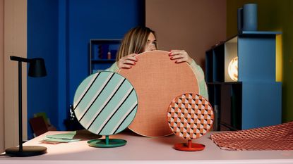 A woman holding patterned speakers in front of her with bold colors also surrounding her