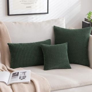 Three dark green throw pillows of different sizes sitting on a couch