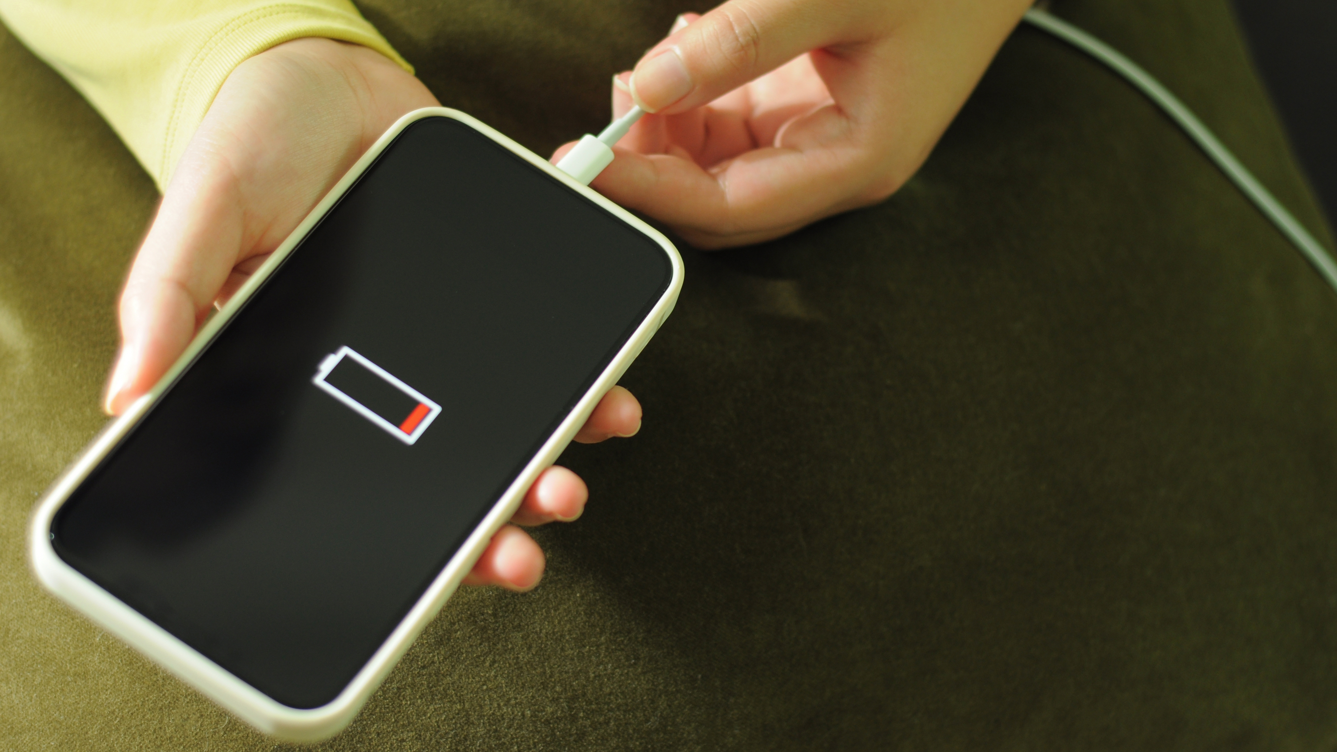 Two hands holding a phone and plugging a charger into it