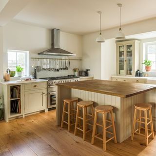 White kitchen walls with wooden floor and island unit and stools