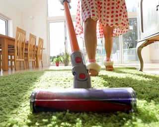 Woman vacuuming fluffy green rug in slippers on a sunny day