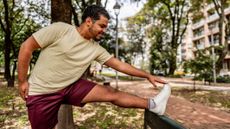 Man stretching in park with foot on backrest of a bench