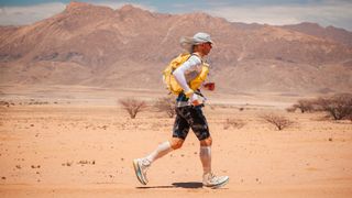 Ultra runner Jon Shield runs across a desert landscape, mountains in the background.