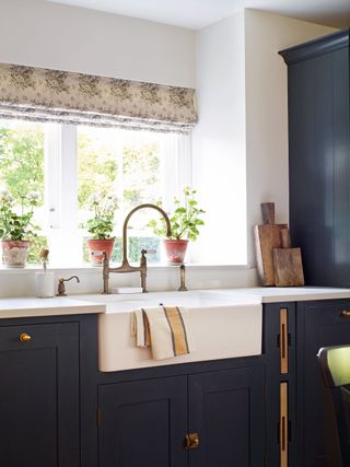 butler's sink by window with floral blind and blue kitchen cabinets