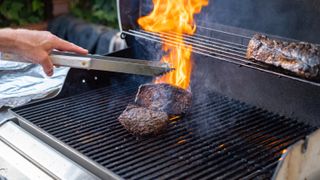 A fire on a grill after flipping beef with tongs