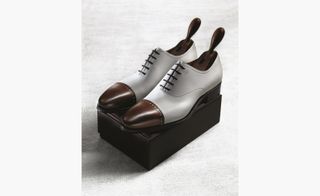 Silver men's smart shoes with brown toes on a black box.