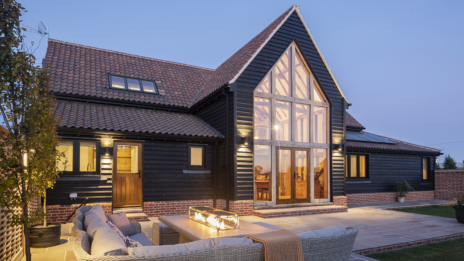 The exterior of a timber frame home lit up at dusk with a contemporary patio garden