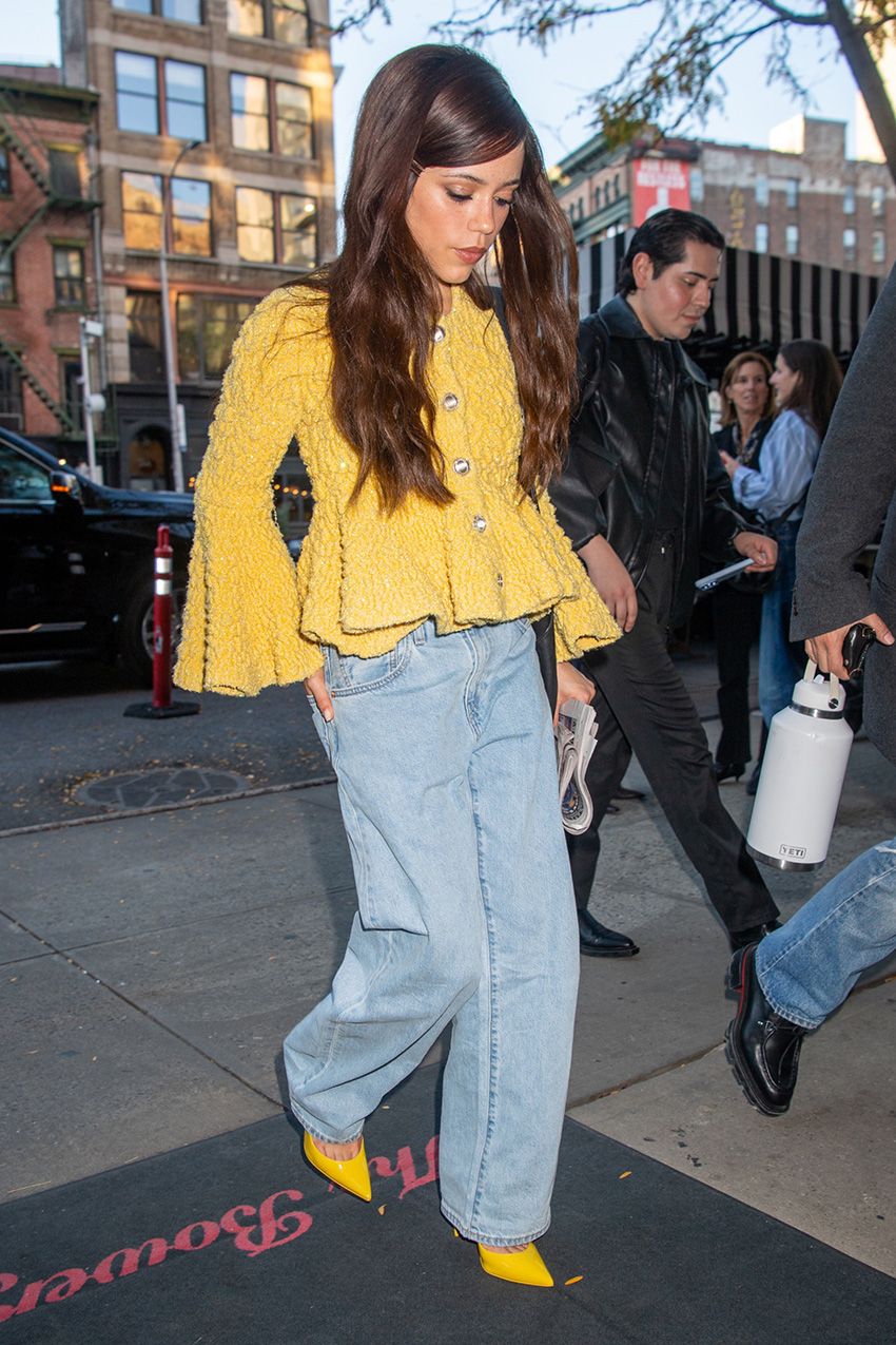 Jenna Ortega wearing jeans, a yellow sweater, and matching yellow pumps.