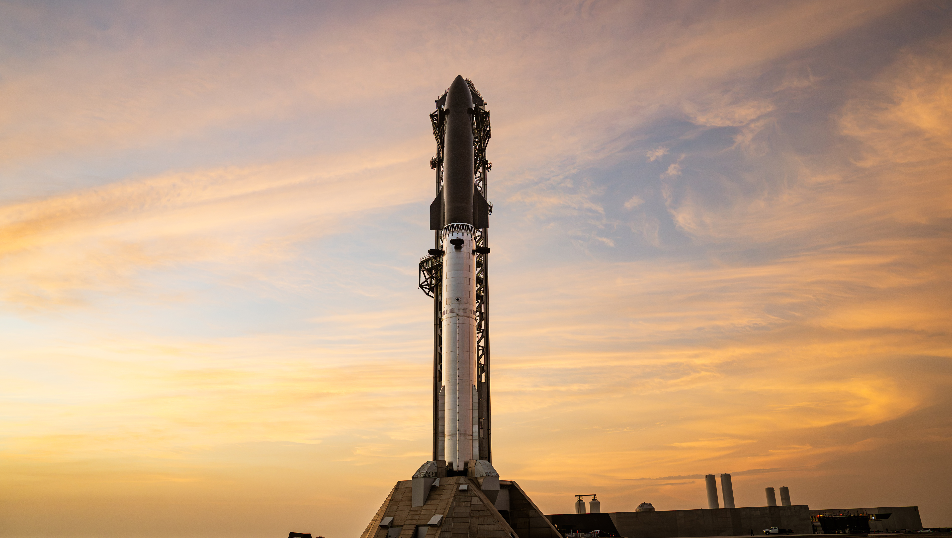 A towering SpaceX Starship rocket stands ready for Flight 13 launch amid a stunning pink sky in twilight.