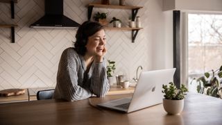 Slack alternatives: Smiling woman using laptop in kitchen