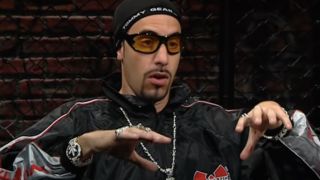 Sacha Baron Cohen, dressed as Ali G, talking in front of a chain link fence on Da Ali G Show