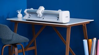 Cricut Venture: everything you need to know; a white craft machine on a desk against a blue wall