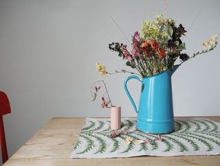 blue jug of dried flowers on a table, small pink vase next to it, red chair on the left