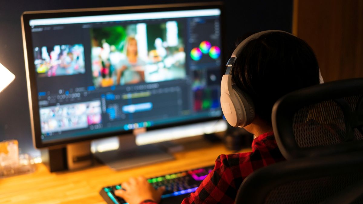 A man wearing headphones using video editing software on a PC