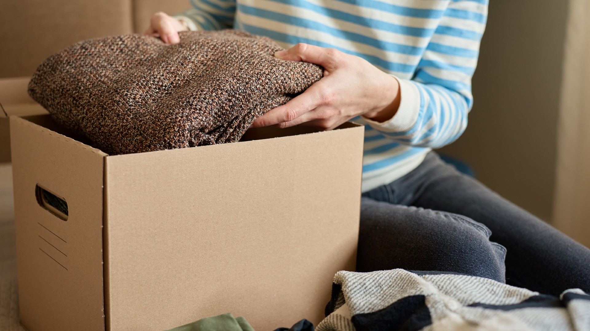 woman putting brown jumper into donation box