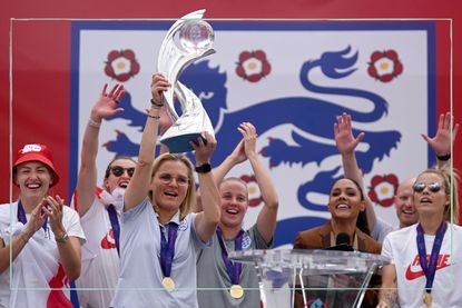 Sarina Wiegman holding up the Euros trophy with the Lionesses cheering behind her