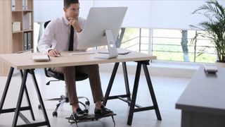 Man using a footrest for under desk while working on computer in office
