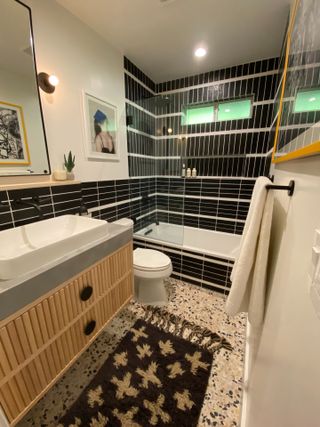 Black tiled bathroom with terrazzo floor, white sink and wall art