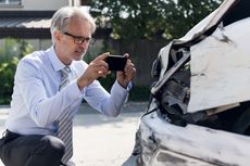 A middle aged man takes photos of damage on car after accident.