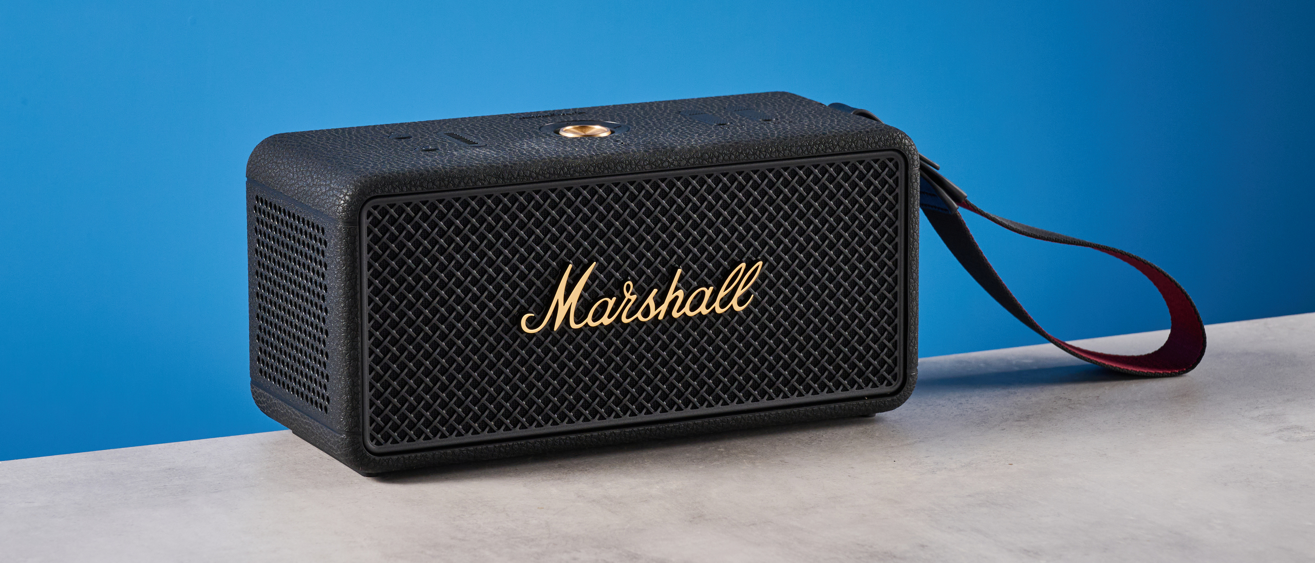 The Marshall Middleton II Bluetooth speaker in Black and Brass, on a stone surface with a blue wall in the background