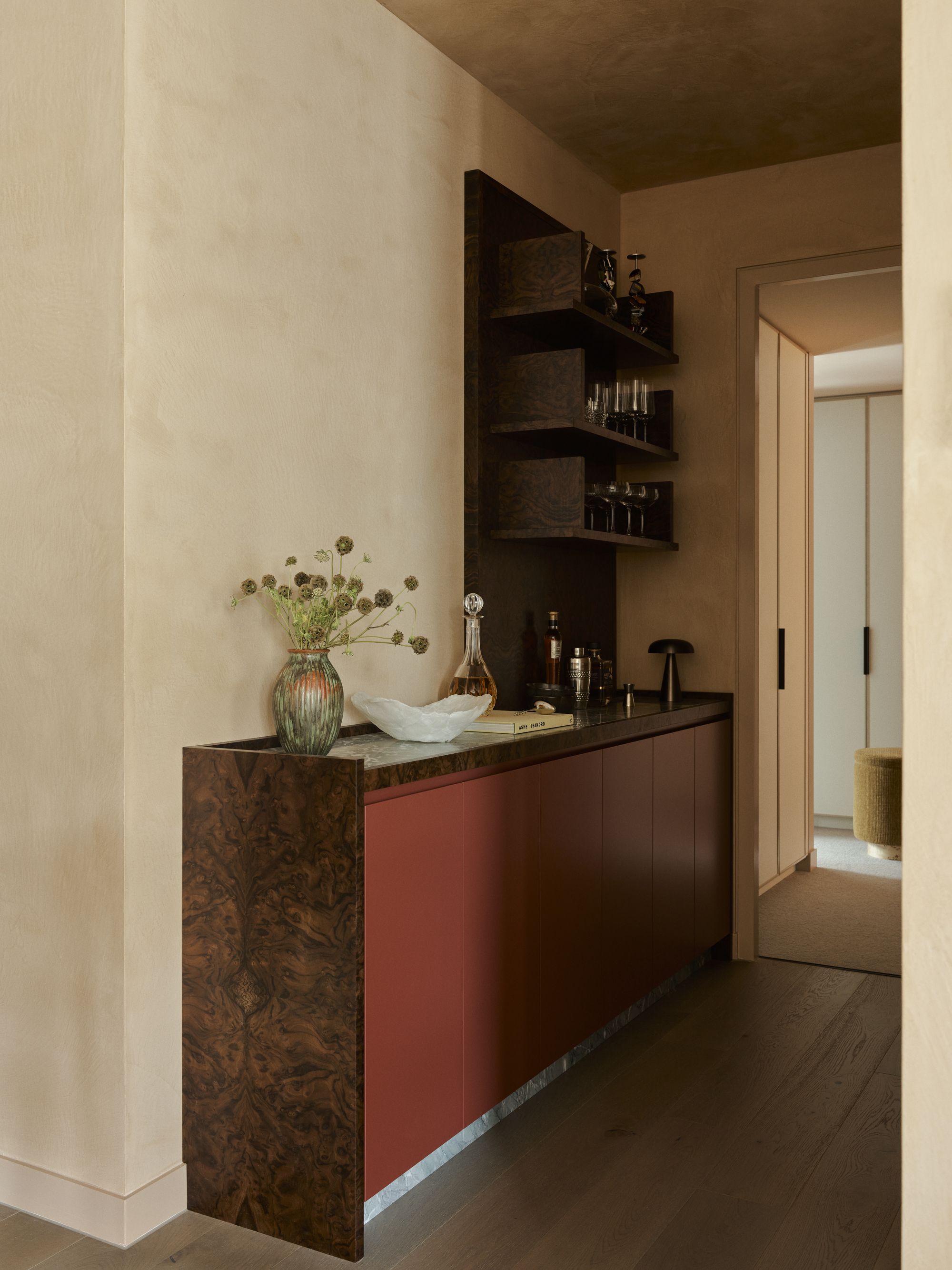 home bar in hallway with burl and red cabinetry, shelves, and plaster walls