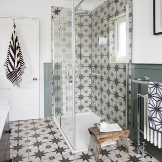Glass shower cubicle with black and white wall and floor tiles, white walls and green wood panels. and wooden stool