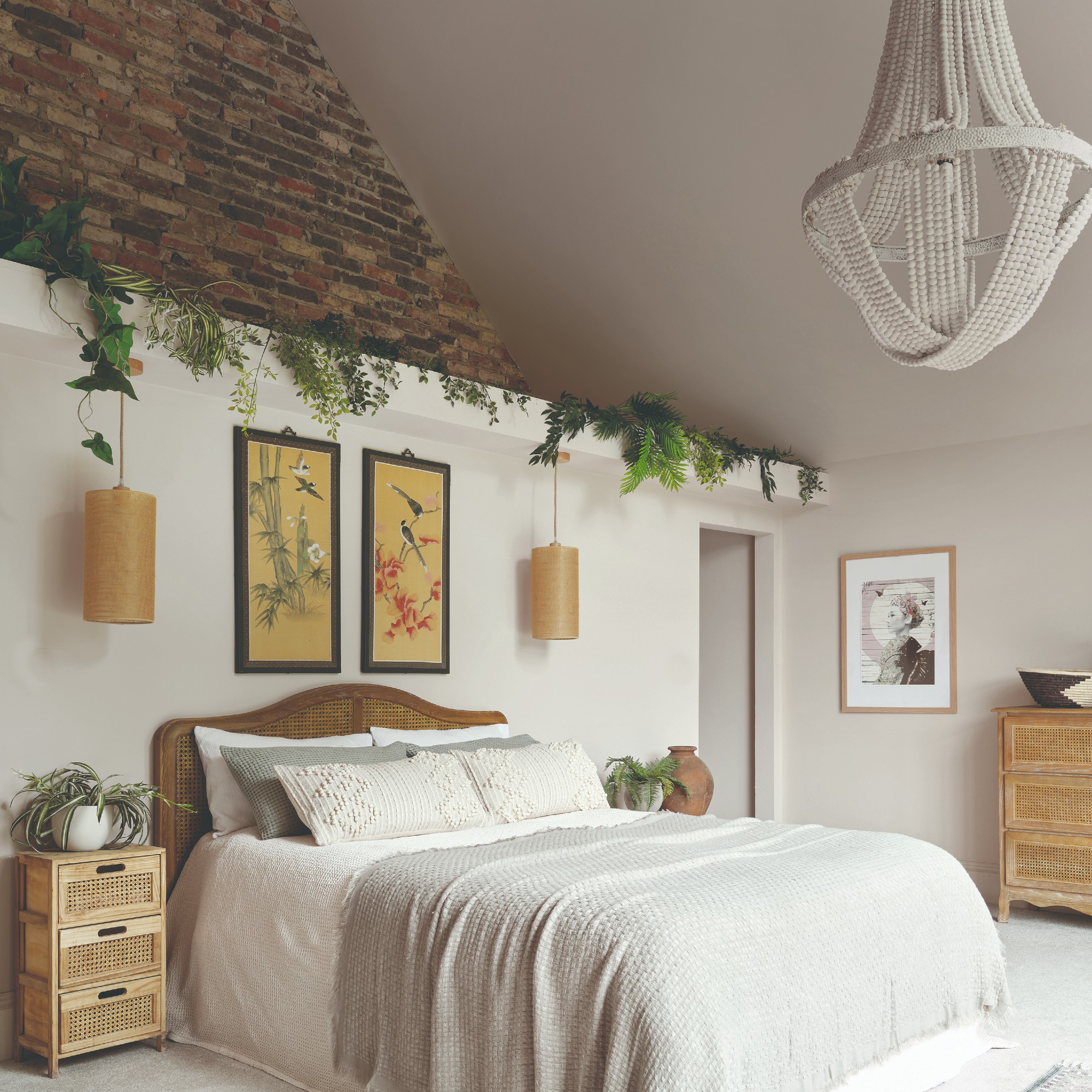 A white bedroom with high ceilings with a chandelier, an exposed brick wall and a rattan headboard