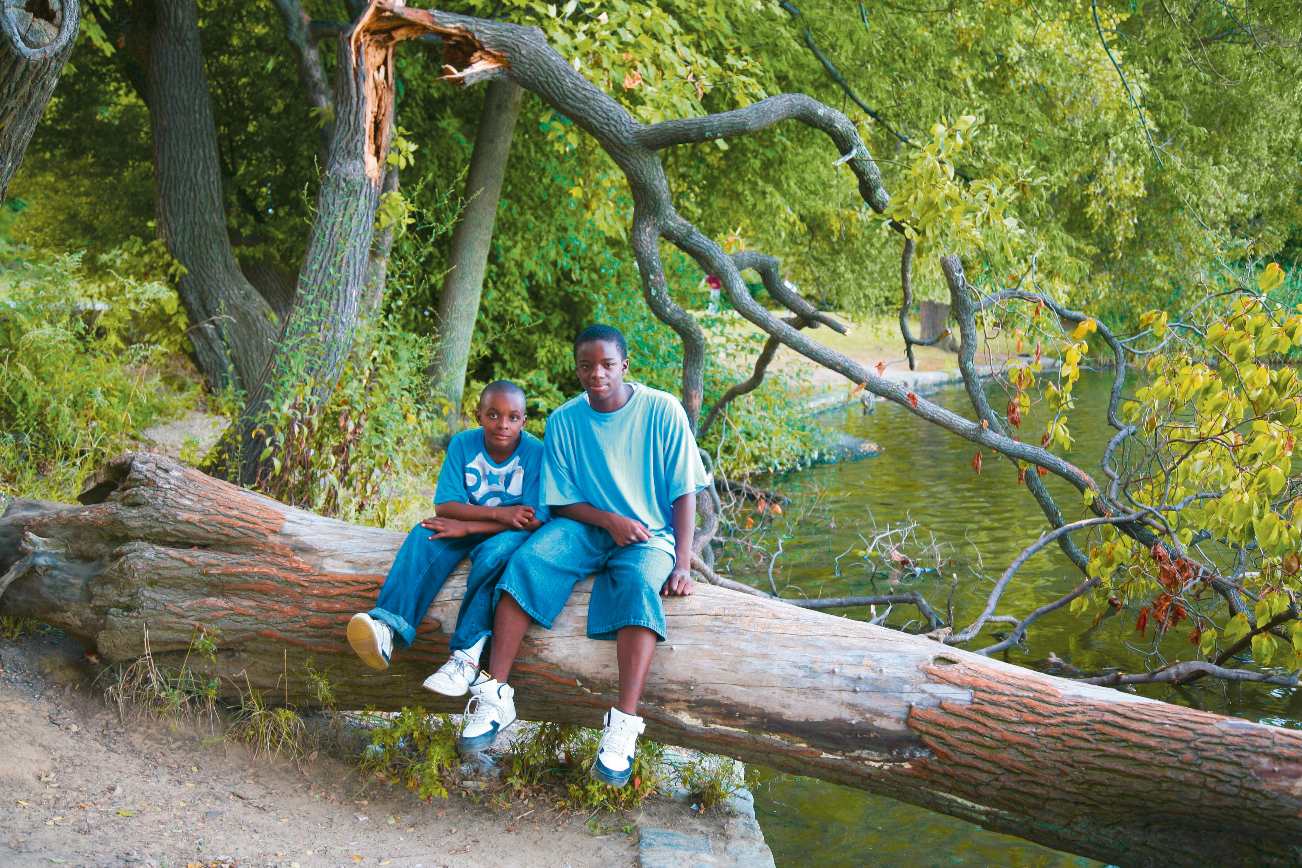 Two boys on a fallen tree beside a lake