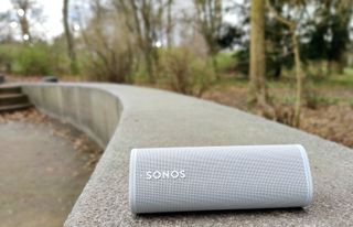 En ljusgrå Sonos Roam ligger utomhus på en betongmur.