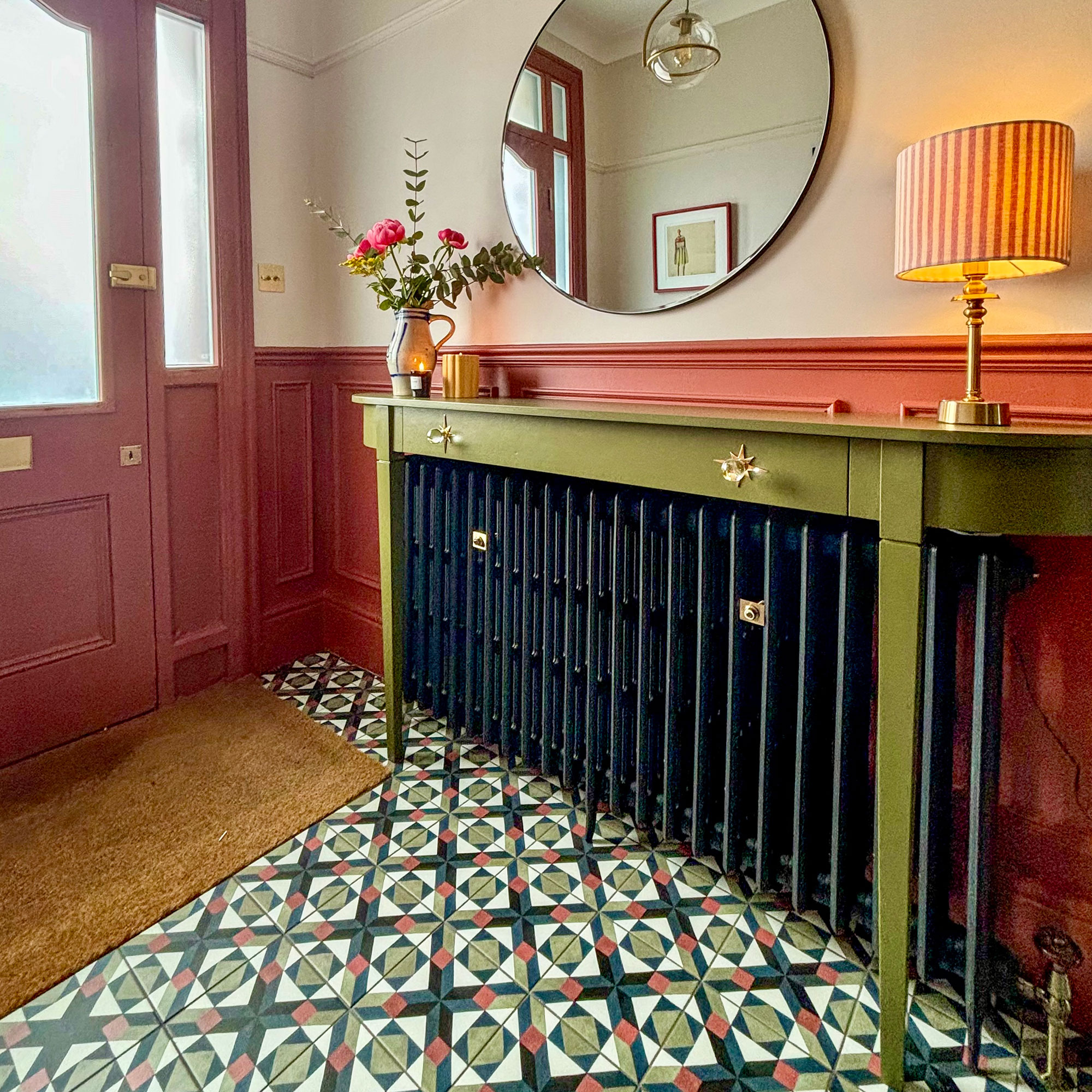 Hallway with coral wall panelling and front door, colourful tiled floor and black radiator topped with slim green sideboard