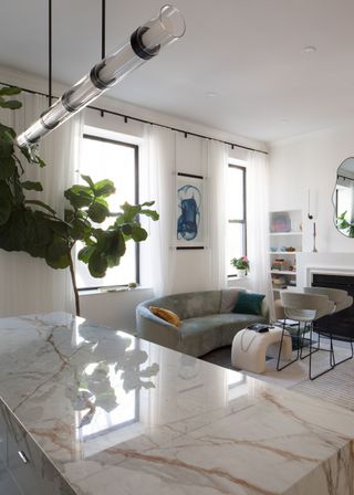 A large kitchen island in an open plan kitchen and living room space. Lighting hangs above the marbles island.