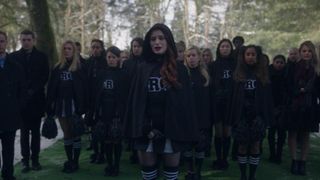 A group of cheerleaders in mourning cheerleader costumes led by Cheryl Blossom look emotional at a funeral