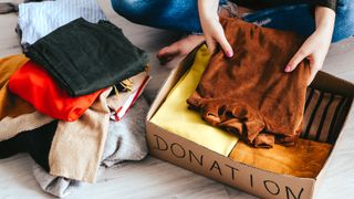 A person decluttering clothes in a cardboard box