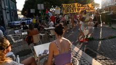 Tourists sit at a cafe while anti-tourism protesters march in Lisbon, Portugal, on June 15, 2025.