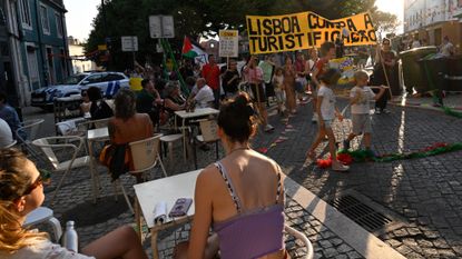 Tourists sit at a cafe while anti-tourism protesters march in Lisbon, Portugal, on June 15, 2025.