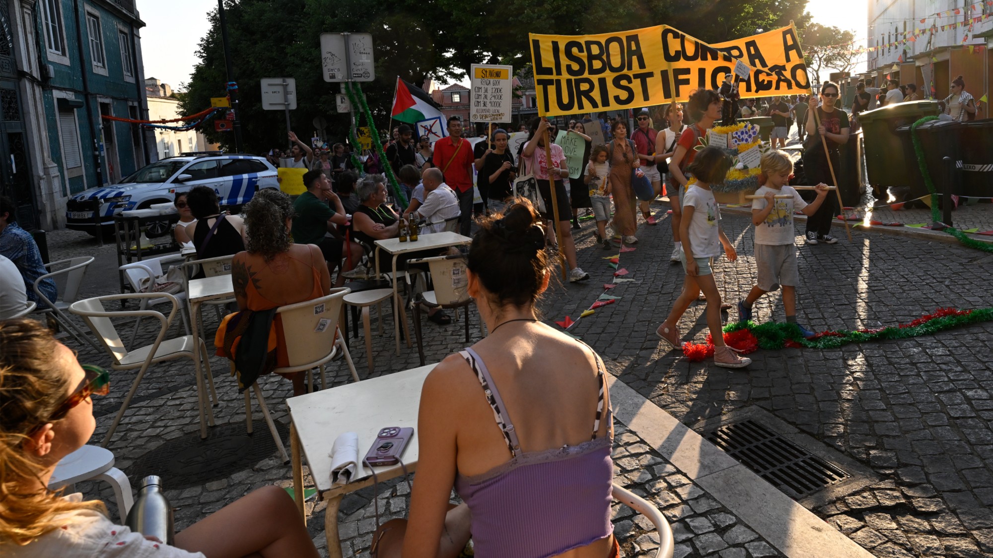Tourists sit at a cafe while anti-tourism protesters march in Lisbon, Portugal, on June 15, 2025.