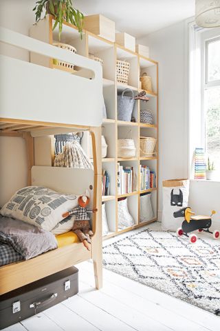 White kid's room with open shelving for clothes and books, bunk bed in light oak and white, and monochrome rug