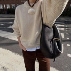 Woman wears cream jumper, brown jeans, carries black Liffner Belted Bucket Bag