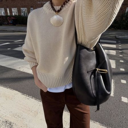 Woman wears cream jumper, brown jeans, carries black Liffner Belted Bucket Bag