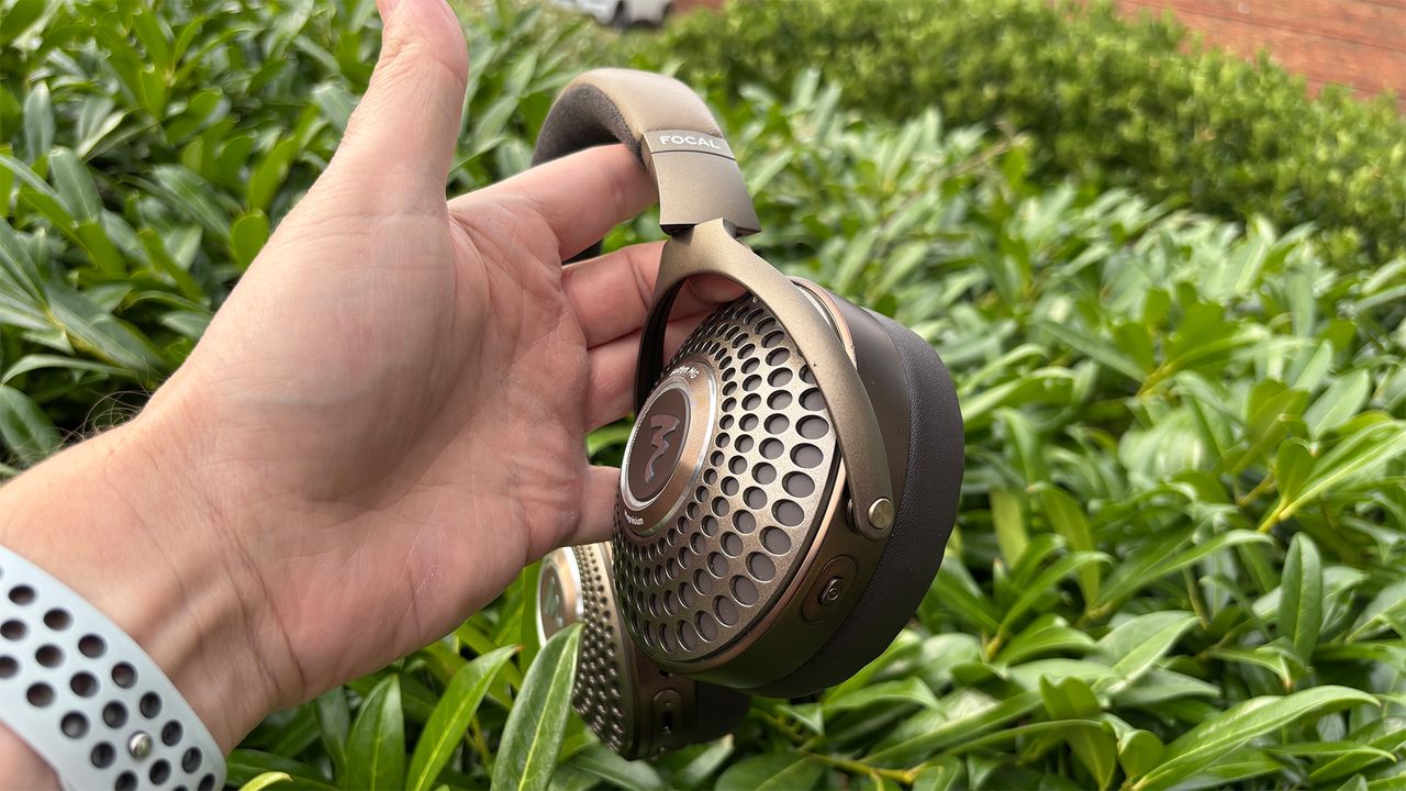 The Focal Bathys MG wireless headphones held side-on in front of a hedge.